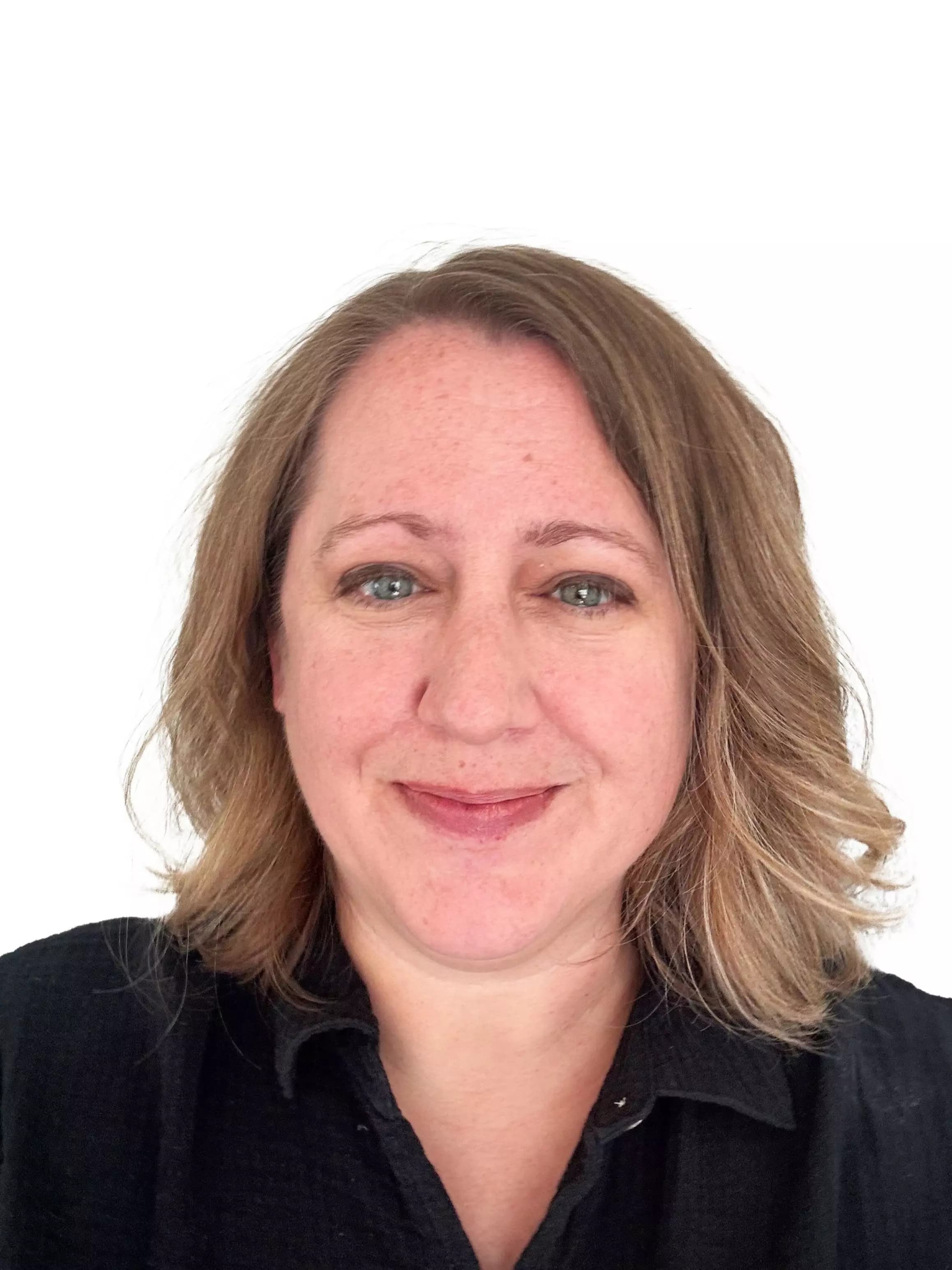 A woman with shoulder-length light brown hair, green eyes, and a subtle smile wears a black collared shirt against a white background.